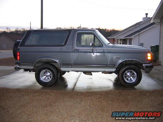 Gray Ford Bronco parked on a driveway, side view. Has a spare tire on the back