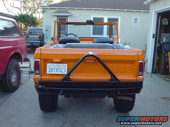 Orange 1977 Ford Bronco rear view, California plates 3AYA523, spare tire carrier, next to a red truck