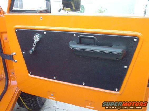 Close-up of an orange vehicle's interior door panel with a black armrest and window crank