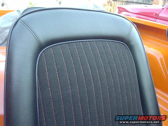 Black vinyl seat with red stitching, orange and red vehicles in background