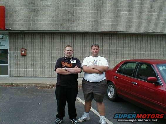 Red 1997 Ford Crown Victoria sedan parked on asphalt, side view, with two men standing nearby