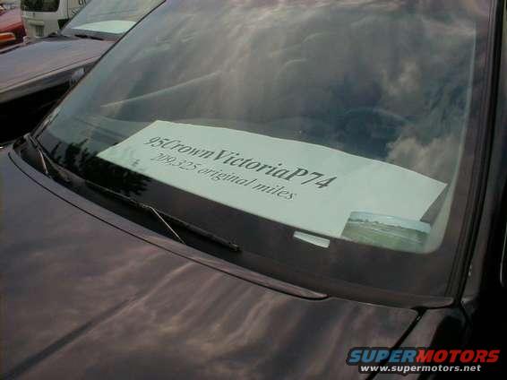 Car windshield with a sign that says 95 Crown Victoria P74, 209,325 original miles. Other cars visible