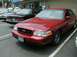 1997 Ford Crown Victoria - A red 1997 Ford Crown Victoria is parked in a lot, showing its front grille and headlights.