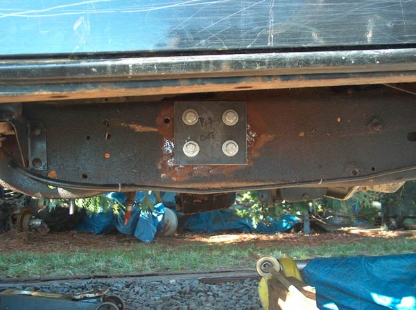Bolted bracket on a rusty vehicle frame. Text on bracket reads 'P.S. DOT'