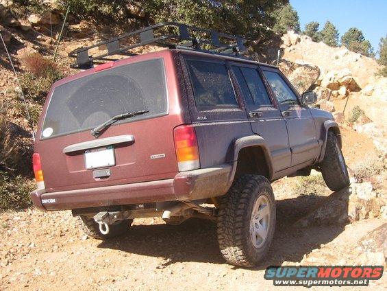 Maroon 2000 Jeep Cherokee on a rocky trail, rear view. It has a roof rack and is angled on uneven terrain