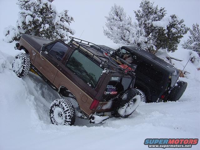1986 Ford Bronco II and a black SUV stuck in deep snow, trees covered in snow in background
