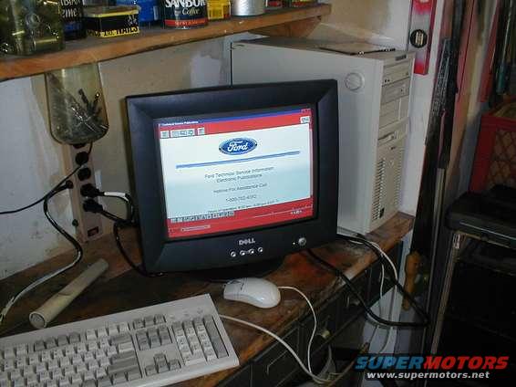 Computer monitor displaying Ford Technical Service Information, with keyboard and mouse