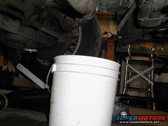 Undercarriage of a vehicle with a white bucket collecting fluid, tire visible