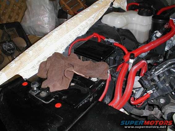 Engine bay with red wiring, battery, and a brown cloth. Supermotors.net logo visible