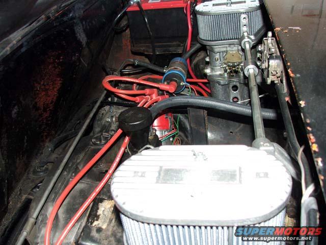 Engine bay showing carburetor, air filter, battery, and red spark plug wires