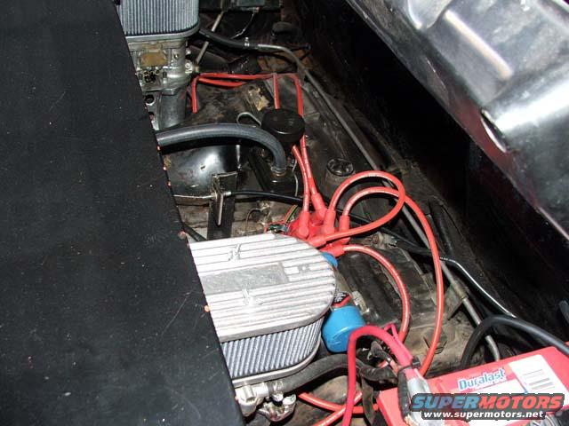Engine bay with red spark plug wires, a carburetor, and a Duralast battery