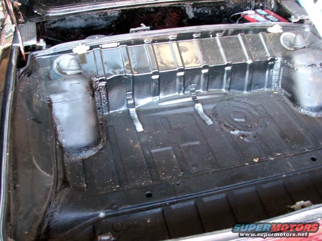 Interior of a car trunk, showing the black painted floor and ribbed sides. A red battery is visible in the upper right