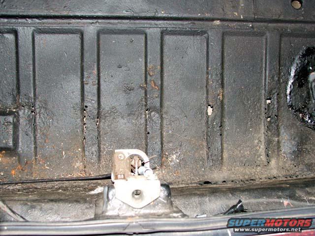 Black car floor with rust and a white latch mechanism