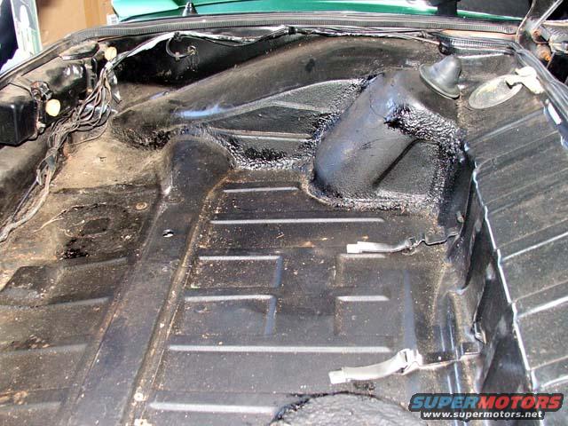 Underside of a car's floor pan with black undercoating and some wiring