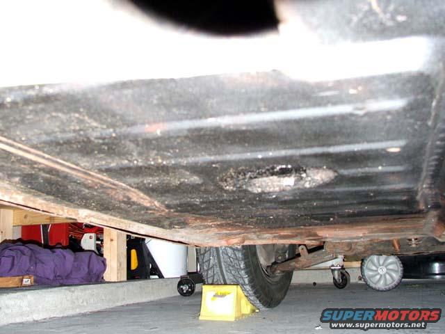 Underside view of a vehicle, showing the chassis and a tire. Some items are stored underneath
