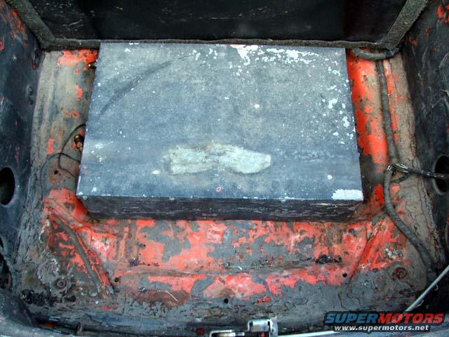 Interior of a car trunk showing a large metal box and rusted orange paint