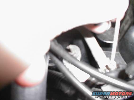 Close-up of engine bay with a hand holding a tool near hoses and wires