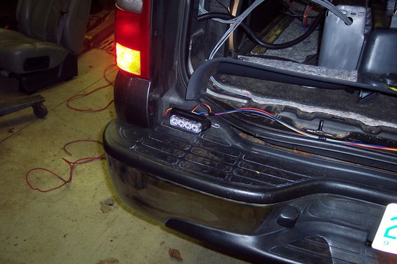 Back of a dark SUV with the taillight on and wires connected to a small light bar on the bumper