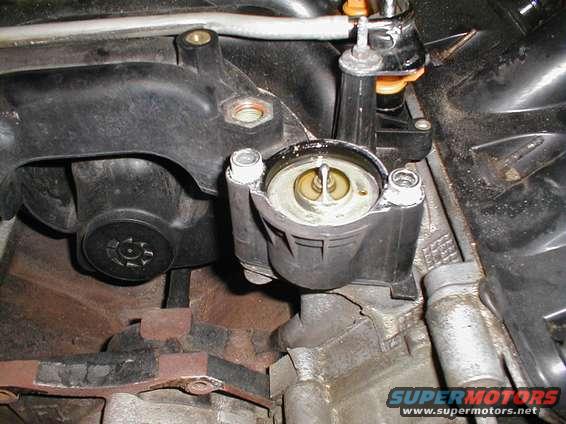 Engine intake manifold and thermostat housing with visible text 'SUPERMOTORS'