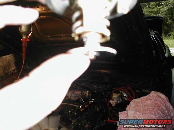 Hand holding a part over a car engine bay. A pink cloth is on the right