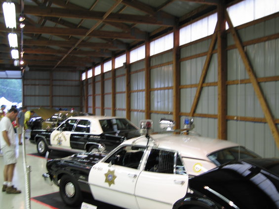 Several police cars parked inside a large garage. One car in the foreground is black and white with a star badge