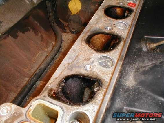Engine intake manifold with four visible ports, showing carbon buildup and oil residue