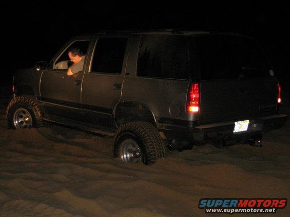 Dark SUV stuck in sand, 3/4 front view. License plate visible