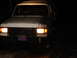 1989 Ford Bronco - Mud-covered 1989 Ford Bronco with headlights illuminated, seen at night.