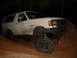 1989 Ford Bronco - A white 1989 Ford Bronco navigates a muddy, off-road terrain at night.
