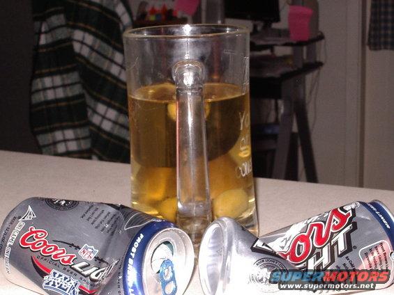 Beer mug filled with amber liquid next to two crushed Coors Light beer cans