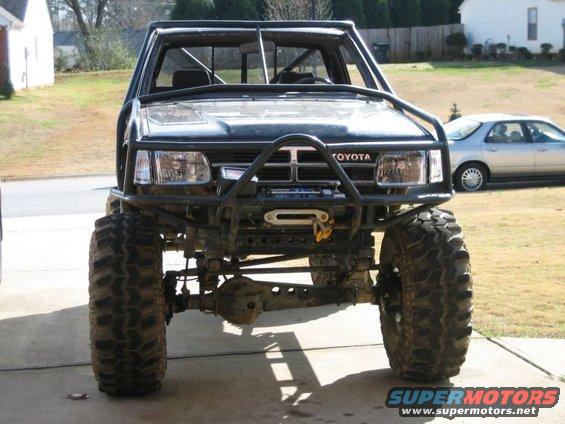 Black Toyota truck with large tires, roll cage, and winch. Front view