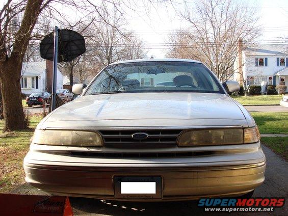 Gold Ford Crown Victoria front view, showing faded headlights and a license plate