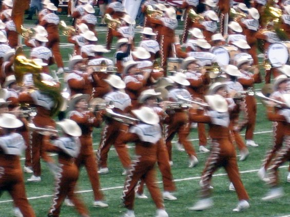 Marching band members in uniform with cowboy hats playing instruments on a football field