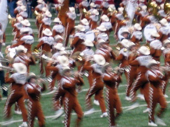 Marching band in orange and white uniforms with cowboy hats on a field