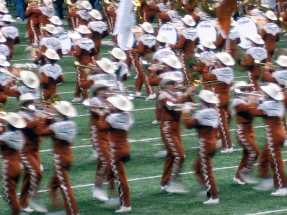 Marching band members in uniform with cowboy hats playing instruments on a football field