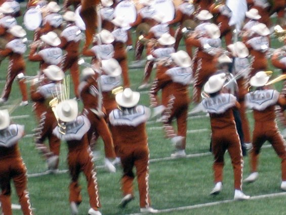 Marching band members in brown and white uniforms with cowboy hats on a football field