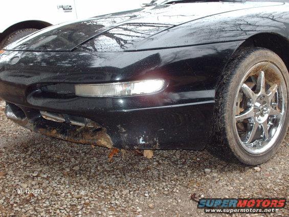 1995 Ford Probe front bumper with damage, chrome wheel, and part of a white Ford F-150 in background