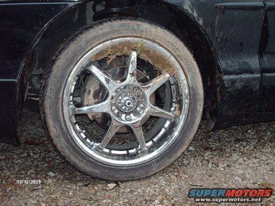 Close-up of a dirty chrome wheel with a tire that has grass and dirt stuck to it. The car body is black