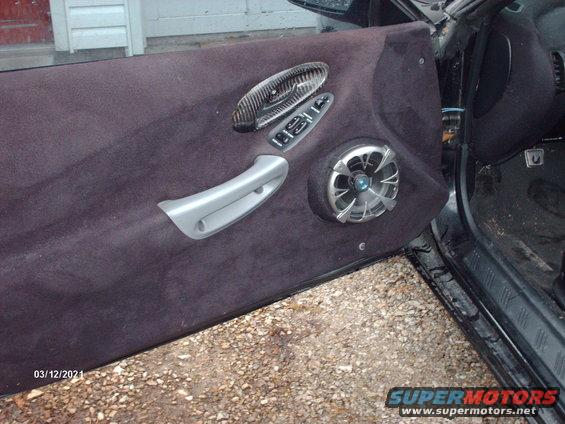 Car door panel with aftermarket speaker and carbon fiber trim on the handle and window controls