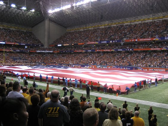 Crowd unfurls large American flag on football field during a game