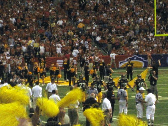 Football game with cheerleaders and players on the field, spectators in the stands