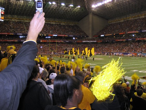 Crowd cheering at a football game, one person holds up a flip phone