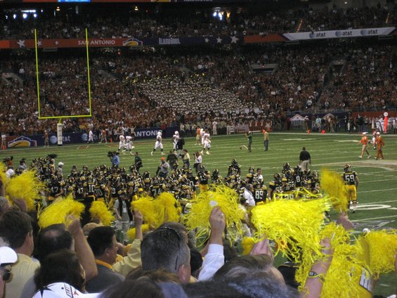 Football stadium crowd with yellow pom-poms, players on field, goal post