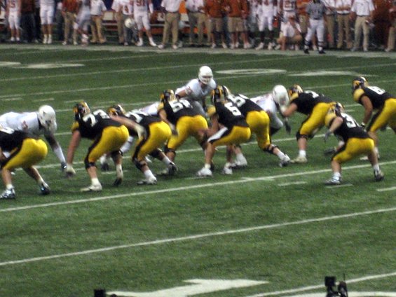 Football players in black and yellow uniforms line up on a green field