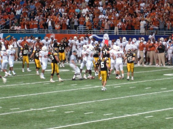 Football players in black and yellow uniforms on a green field with spectators in the background