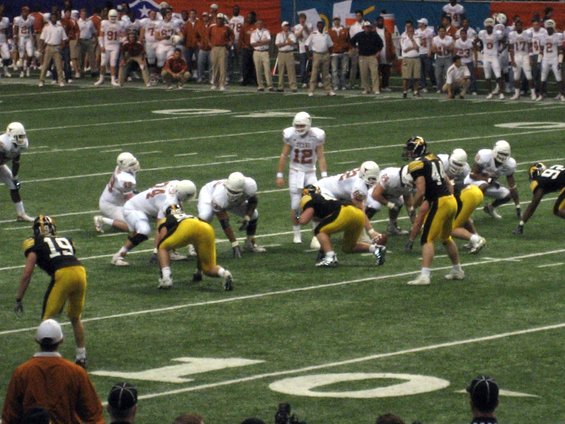 Football players in white and yellow uniforms on a green field during a game