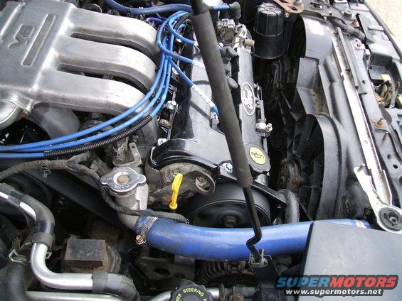 Engine bay of a 1997 Ford Probe, showing the V6 engine, blue spark plug wires, and a large fan