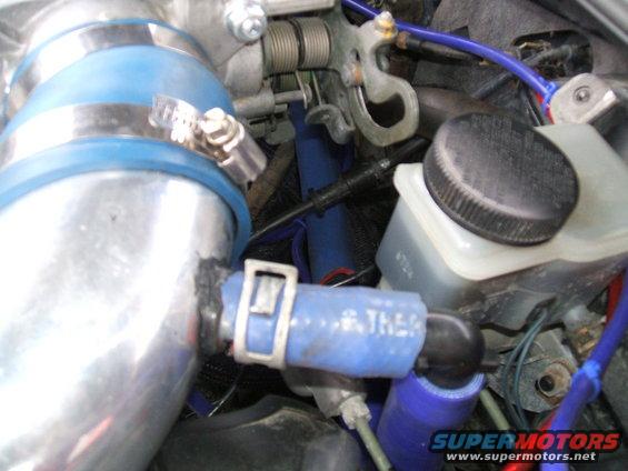 Close-up of engine bay hoses and fluid reservoir with visible text 'THERMO' and 'SUPERMOTORS'