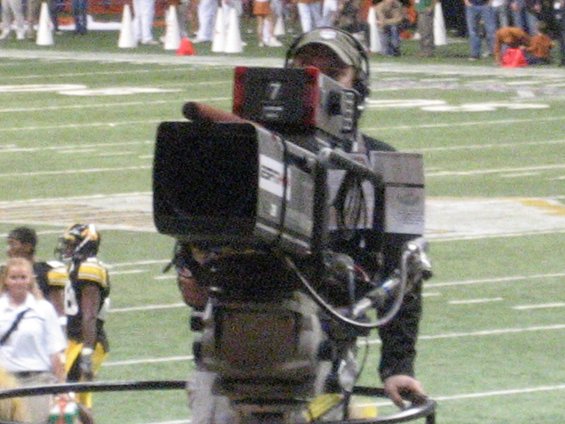 TV camera operator on football field, players in background