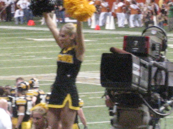 Cheerleader with pom-poms on football field, camera crew in foreground
